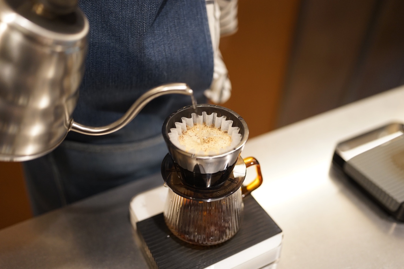 Hot water pouring over grounds in a ceramic dripper set on a glass carafe at Nylon Coffee Roasters