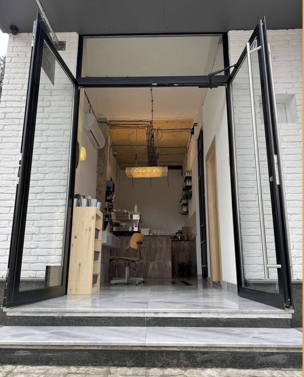 The open black framed entrance of Coffee Syndicate, looking down a narrow marble floored counter toward the espresso machine