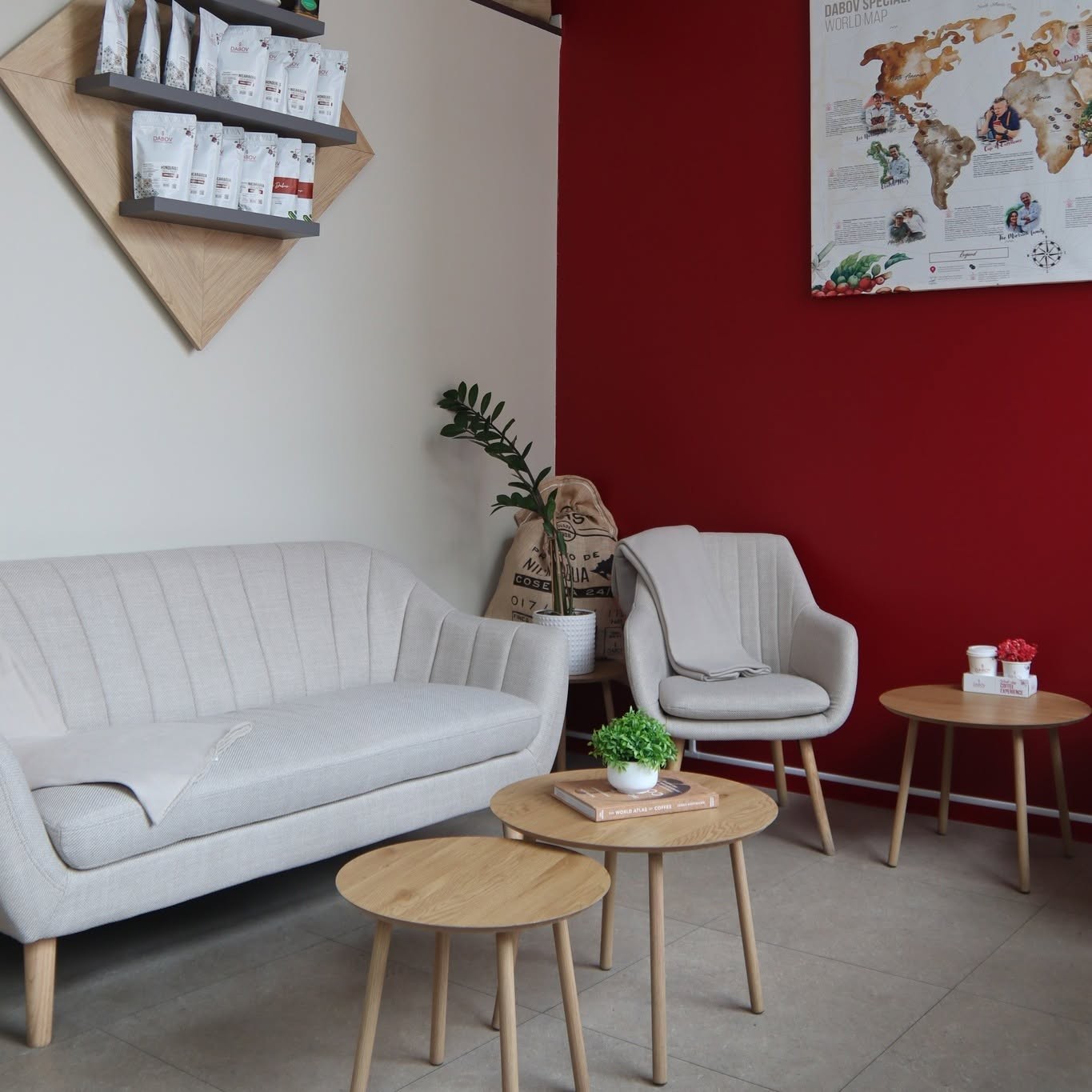 A lounge seating area at DABOV with a cream sofa and armchair, a shelf of retail coffee bags, and a world map poster on a red accent wall
