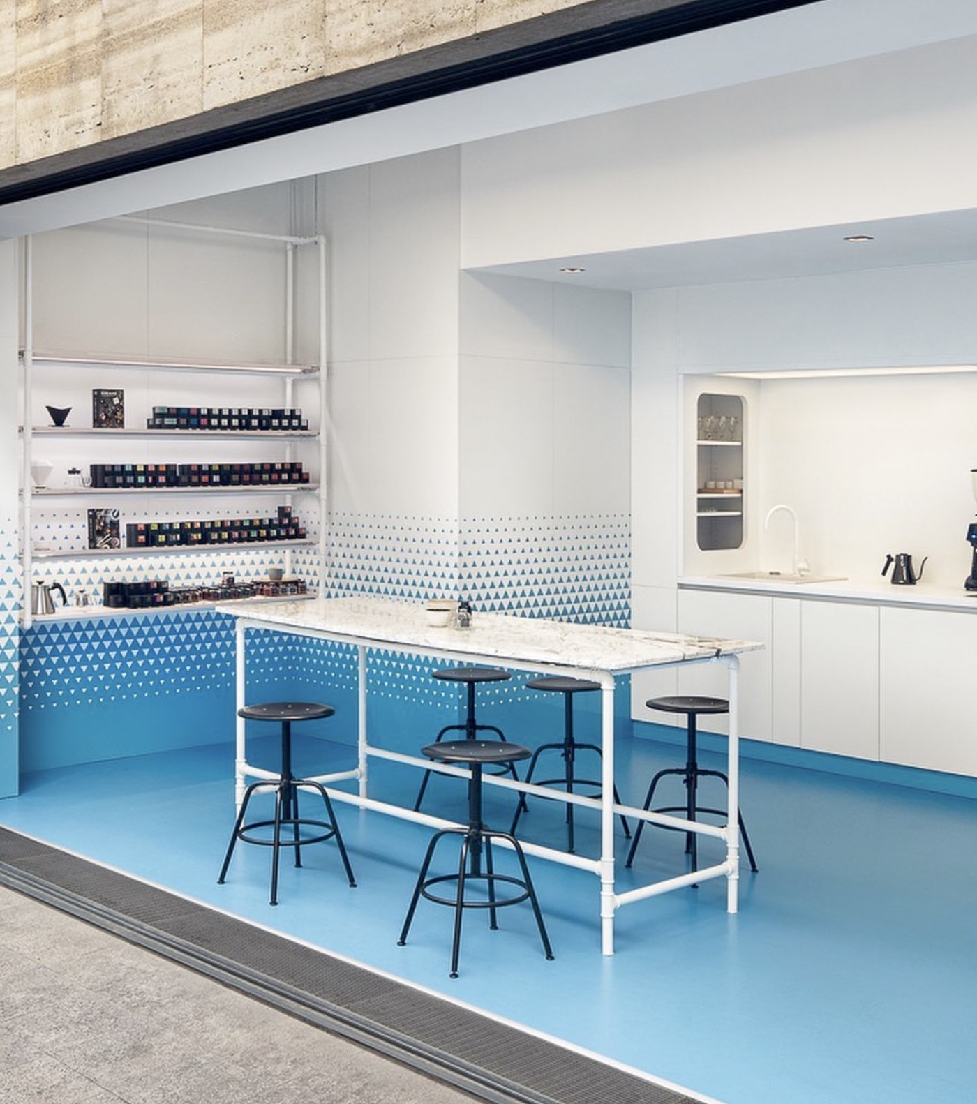 A blue tiled brew bar with a marble counter and black stools facing an open kitchen at Drekka