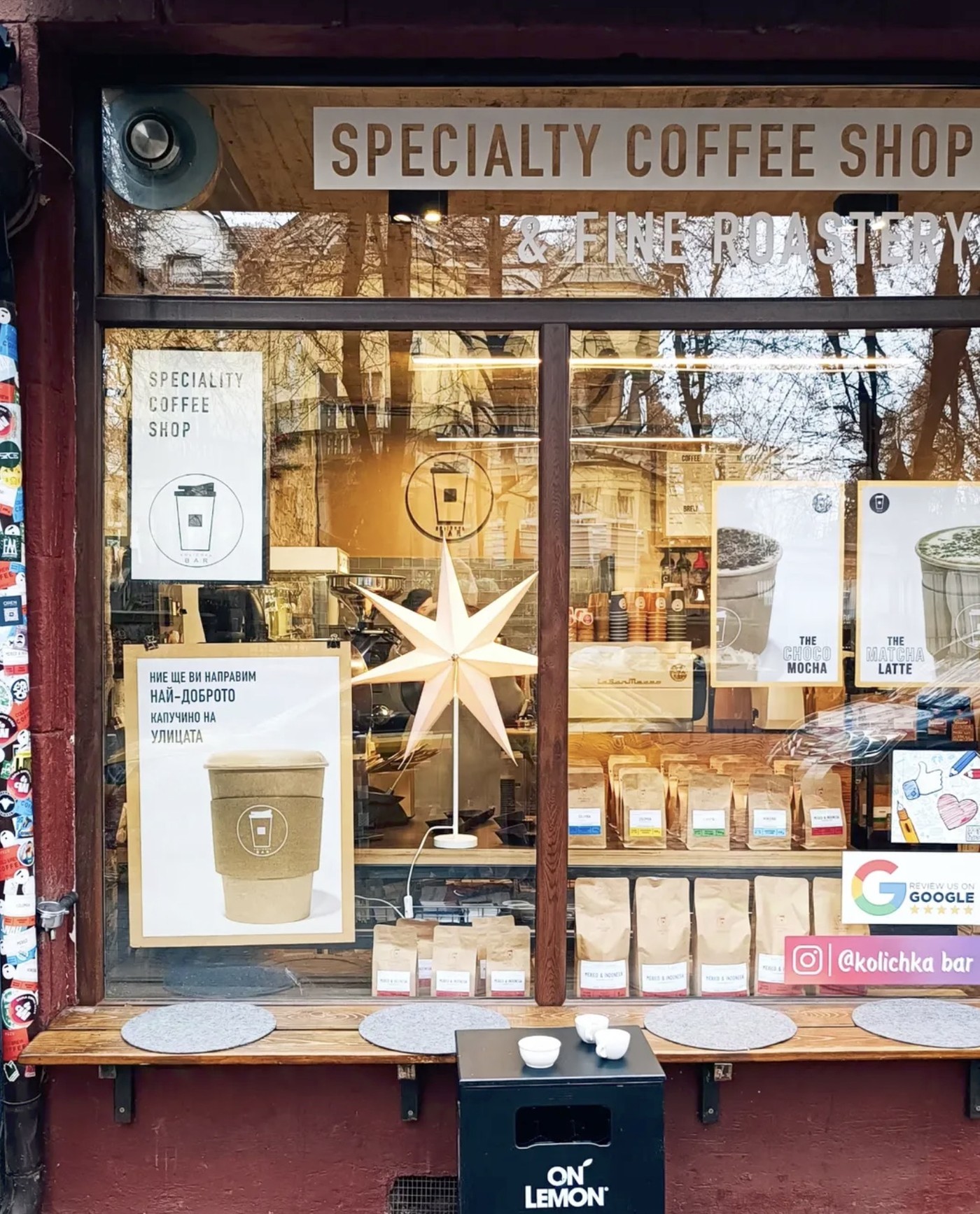 The window front of Kolichka Bar, shelves of retail coffee bags and a paper star lamp visible through the glass