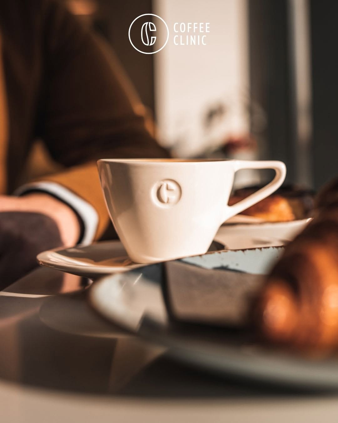 A branded Coffee Clinic cup and saucer with a croissant on the table