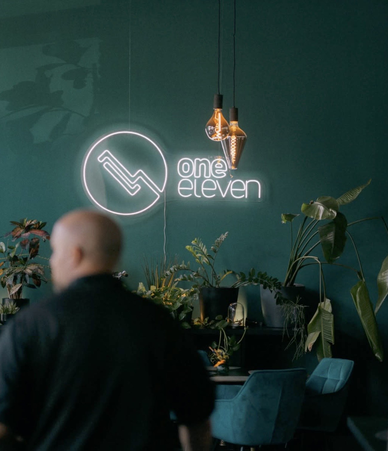 The neon One Eleven sign glowing on a teal wall above plants and pendant lights