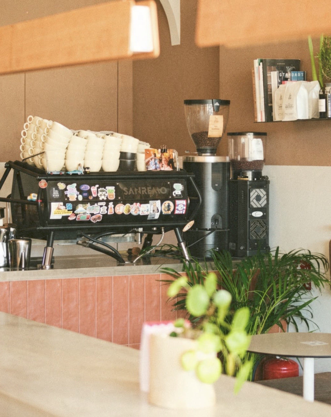 A sticker covered Sanremo espresso machine and grinders beneath a shelf of coffee books and retail bags at Utopia
