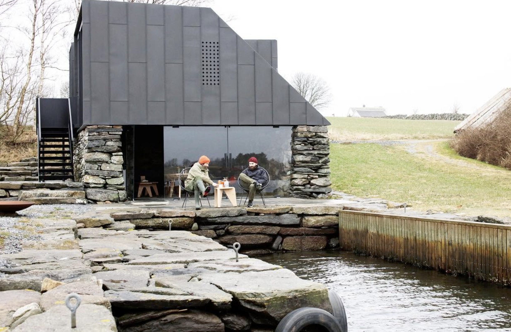 A stone and dark metal clad building beside water, an Atelier Kokko architecture project