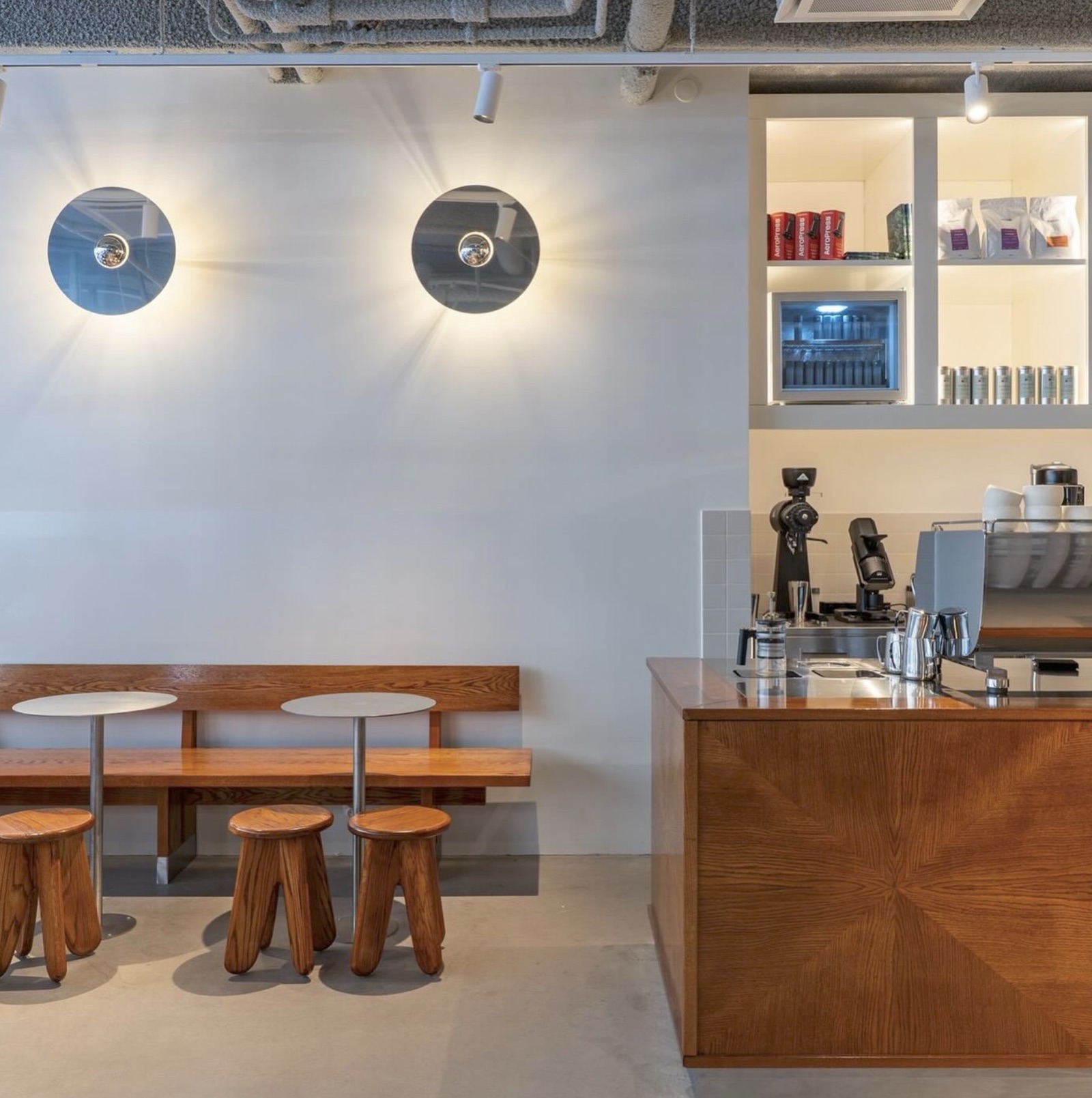 The minimalist dining area at Cafe Pascal, round mirror sconces above a wood bench and stools, retail shelves by the counter