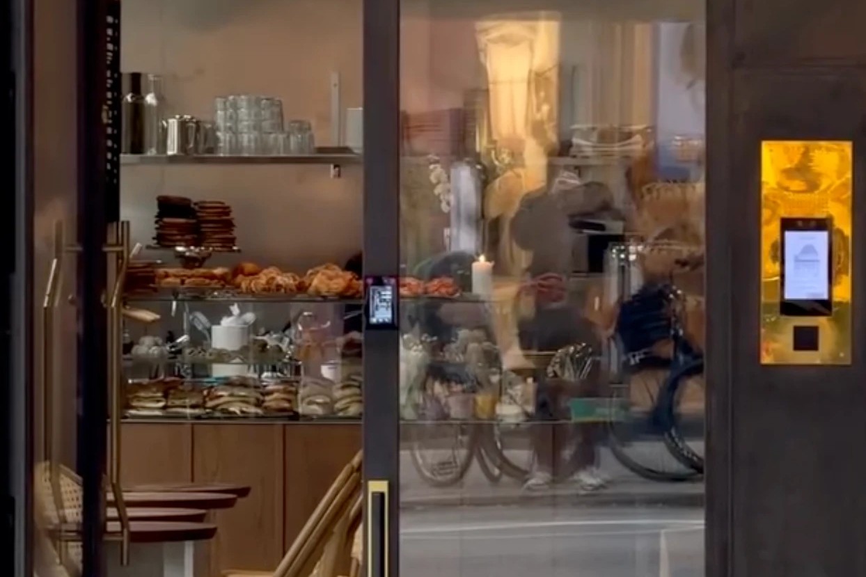 The pastry case and entrance at Cafe Volta Hagastaden, glasses and stacked cups on the shelf above trays of sandwiches and baked goods