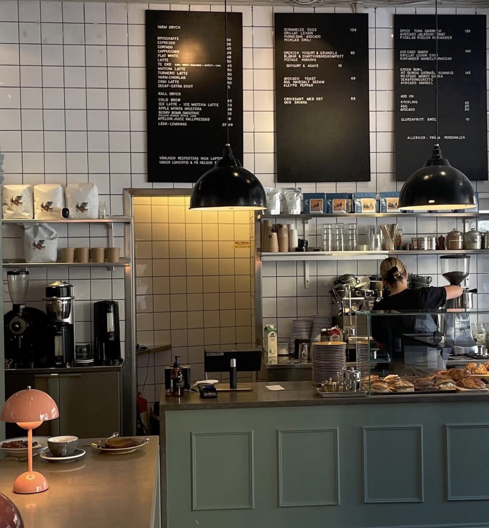 The tiled counter and menu boards at Kaffeverket, pastry case up front and a barista working the espresso bar