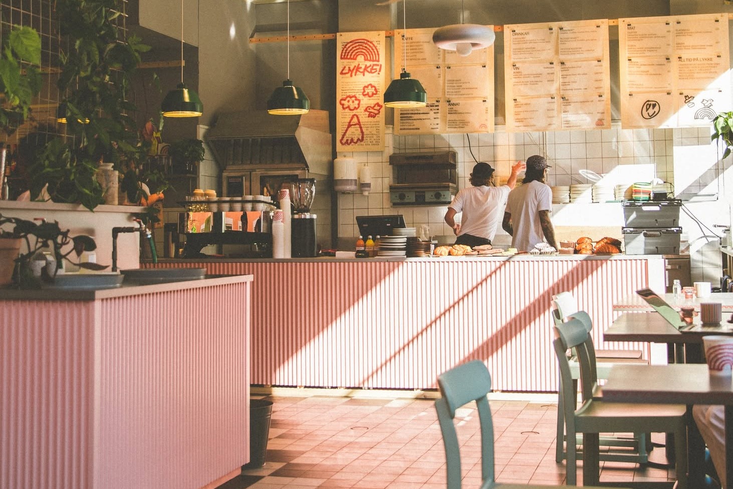 The pink corrugated counter and hand lettered menu boards at Lykke Nytorget, with staff working behind the counter