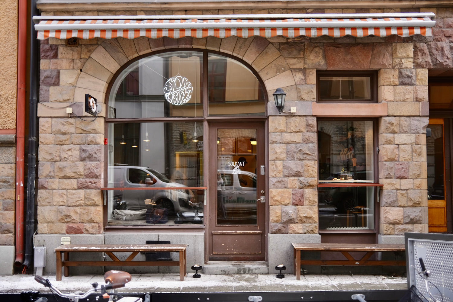 The stone facade and striped awning of Solkant Cafe & Roastery on Pipersgatan, with a neon sign in the arched window