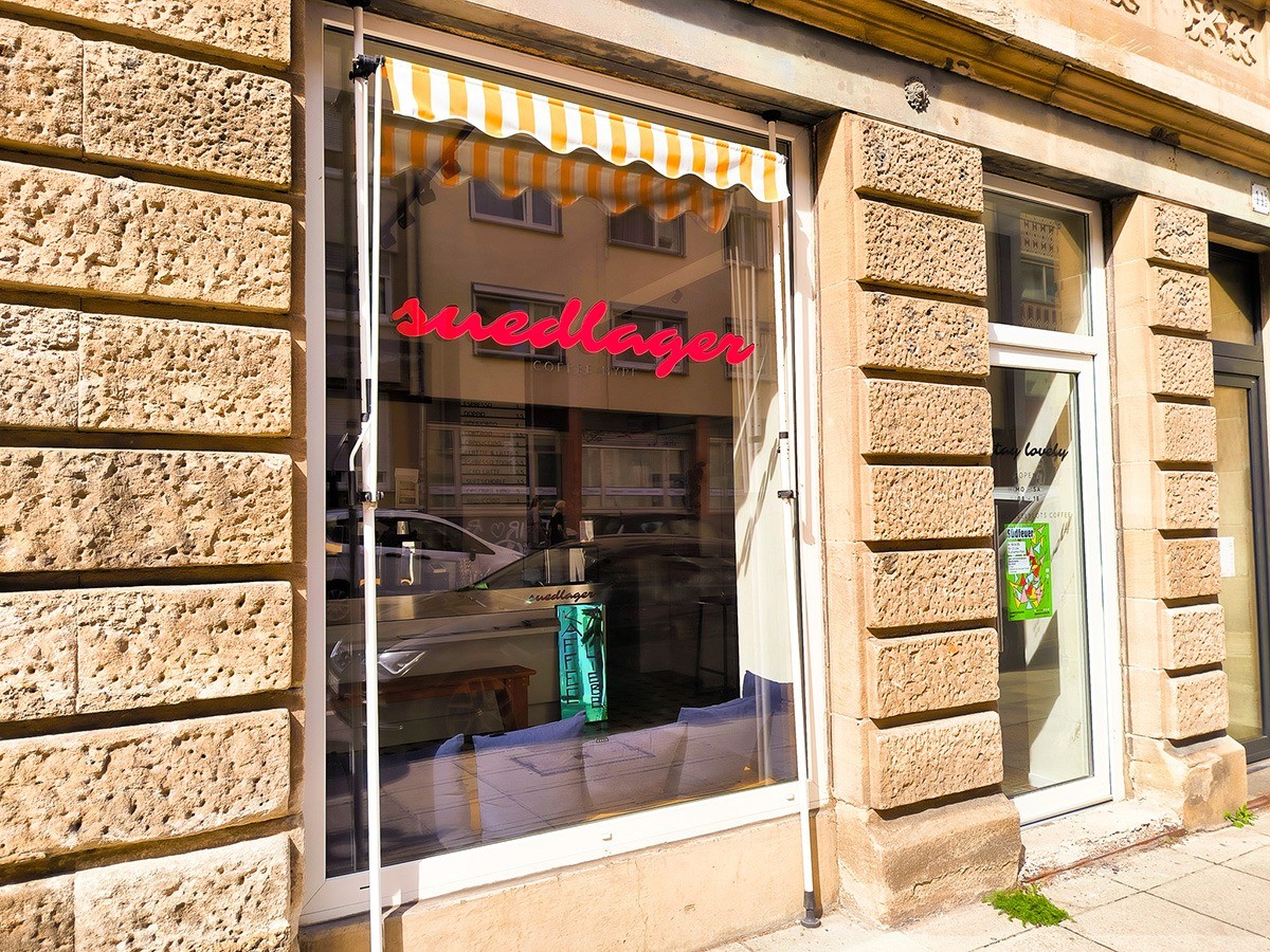 The sandstone storefront of Suedlager, its window framed by an orange and white striped awning and lit up red neon script signage