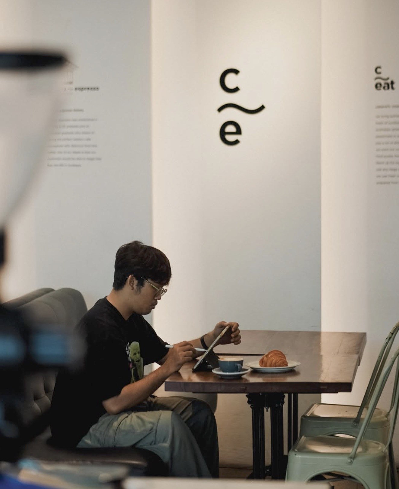 A customer working on a tablet at Caturra Espresso with a coffee and croissant on the table and the C~e logo on the wall behind