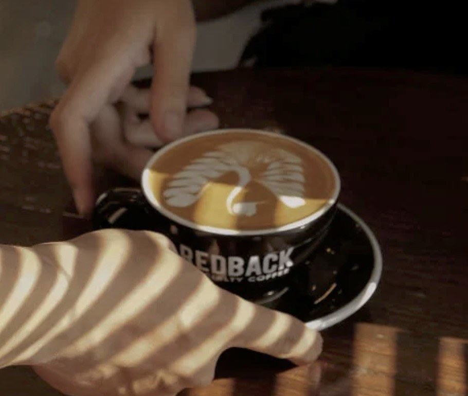 A latte with bird shaped latte art in a branded Redback Specialty Coffee cup on a wooden table