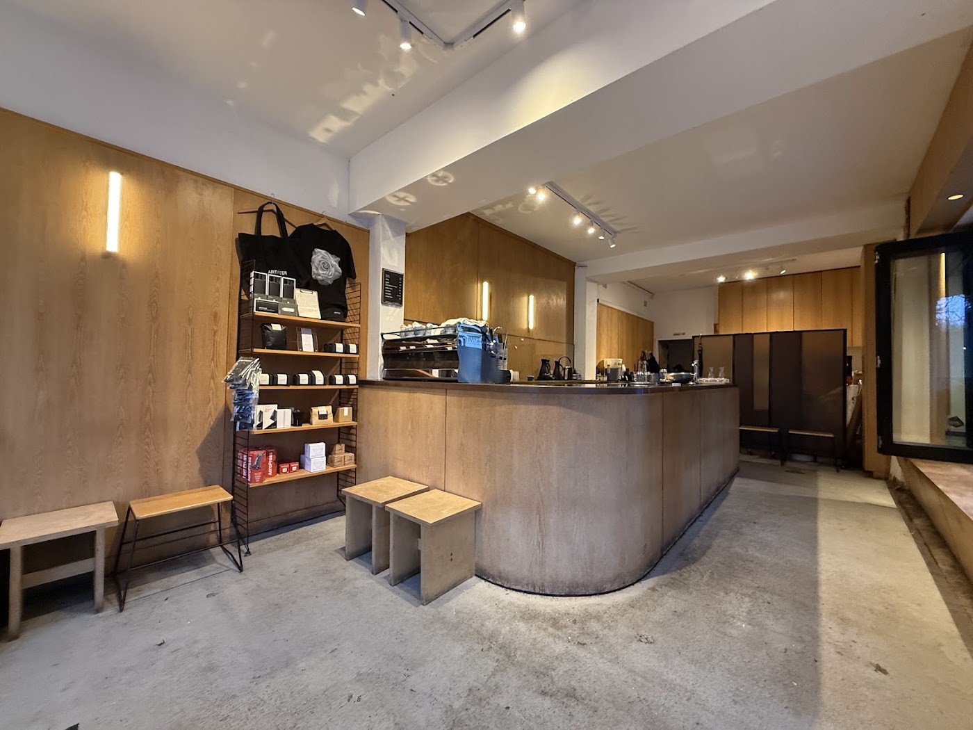 The curved plywood counter and espresso machine at Artificer, with branded tote bags and retail coffee on shelving nearby