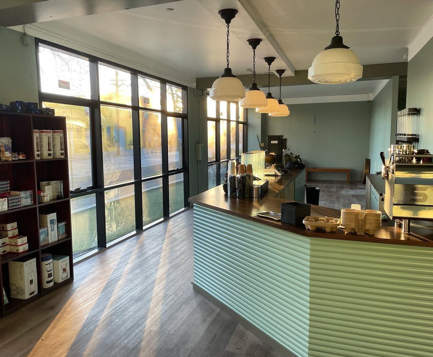 The bright Sydenham Road interior of Coffee Alchemy with ribbed pastel green counter, pendant lights, and a shelf of home brewing gear