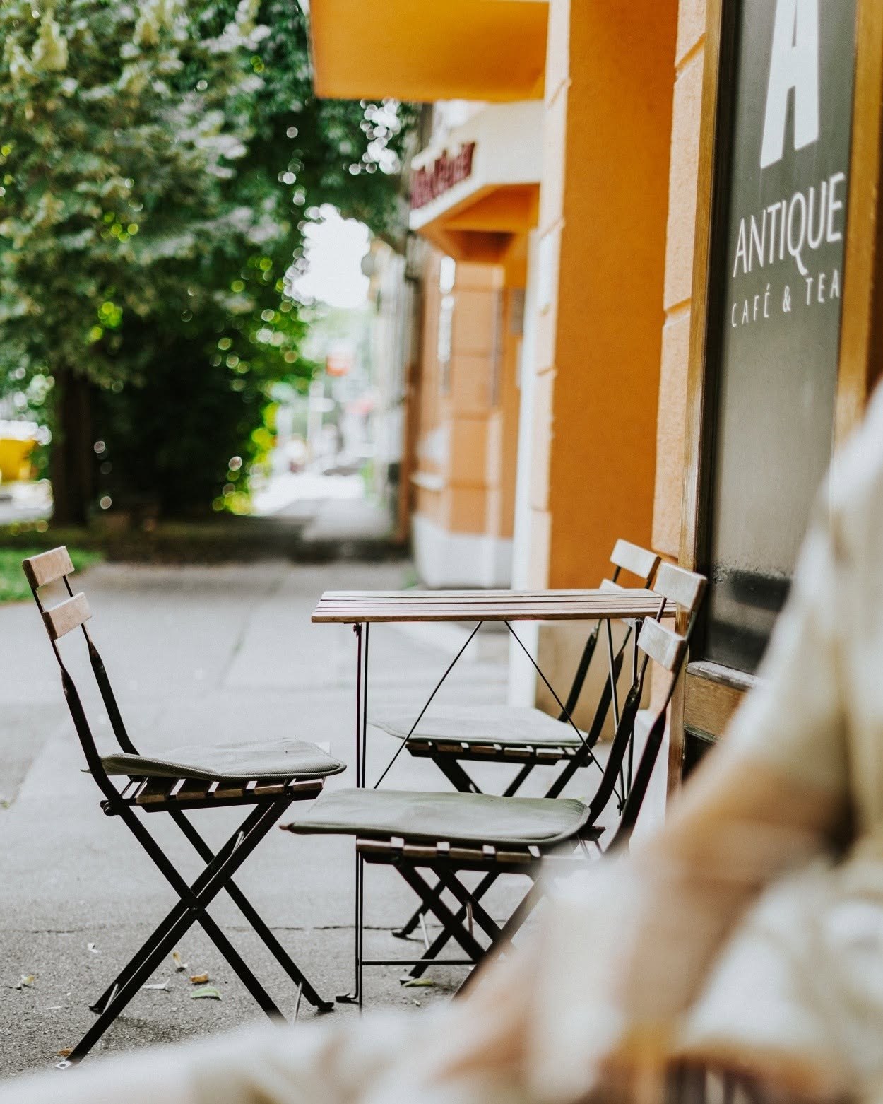 The Antique Cafe and Tea storefront sign above outdoor bistro chairs and a small table
