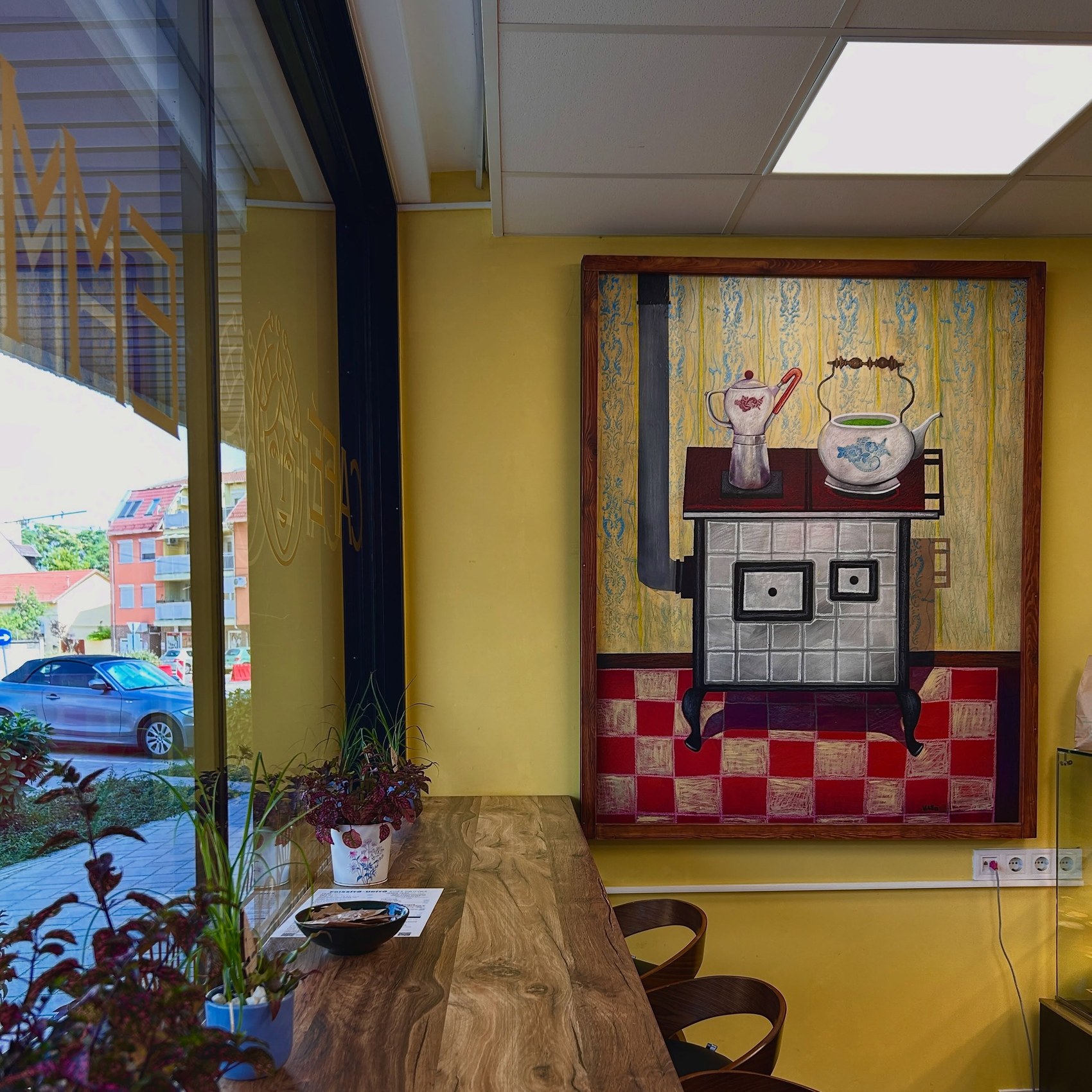 Emmarozs interior with a large decorative stove painting behind the wooden counter, potted plants and yellow walls