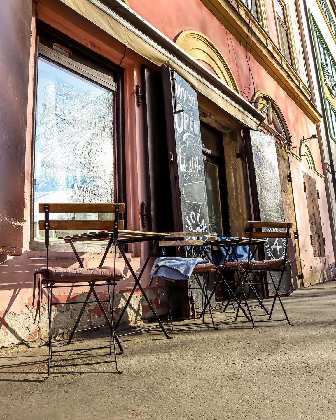 The Hét Kávézó storefront with hand lettered coffee origin windows and an outdoor table and chairs