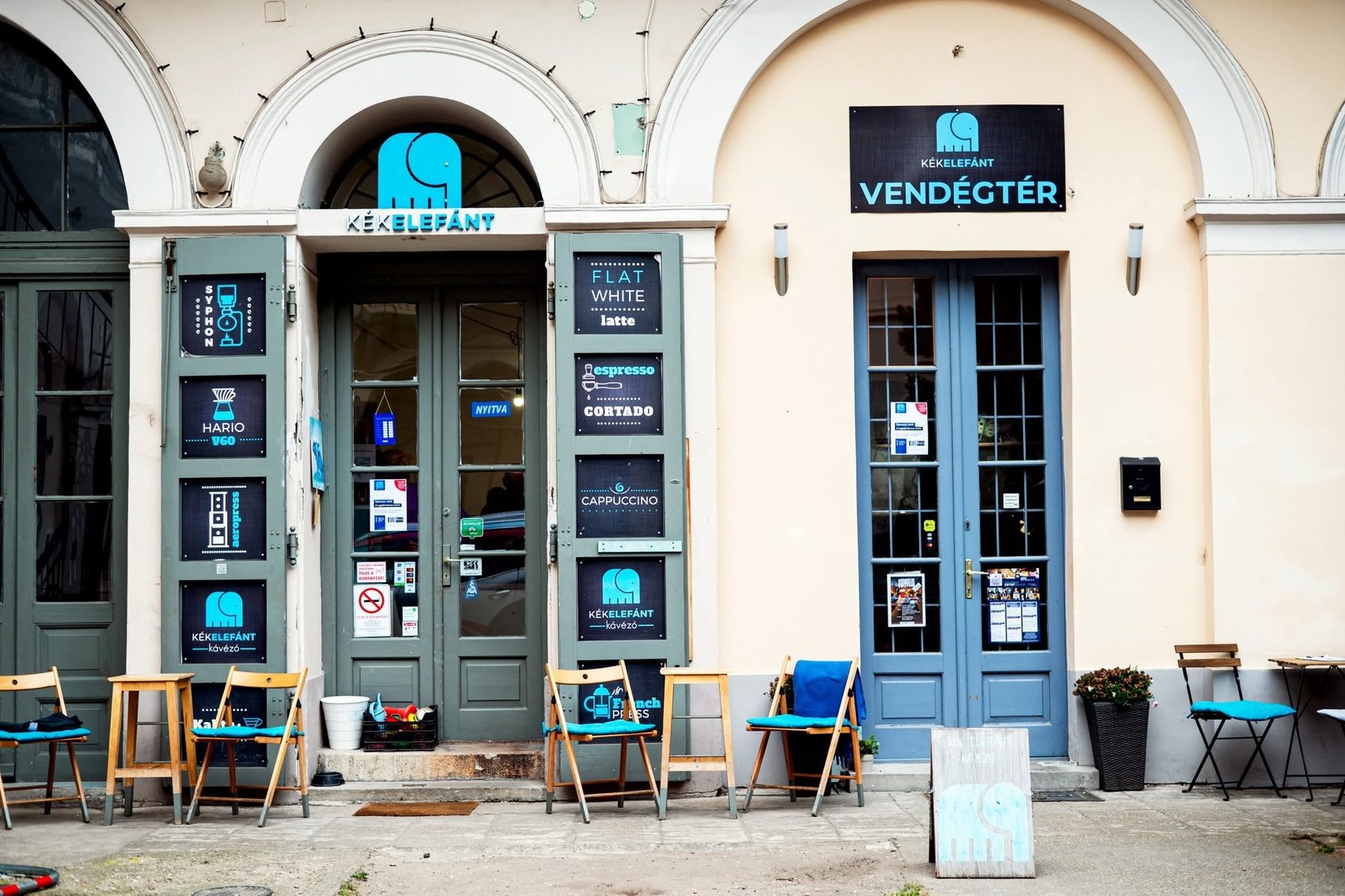 The Kék Elefánt Kávézó storefront with brewing method signage for syphon, Hario V60, aeropress and french press on the doors