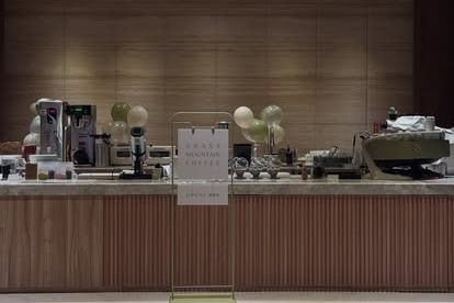 The wood paneled counter at Grass Mountain Coffee's new Shilin shop, with a GRASS MOUNTAIN COFFEE sign card on the bar and pale balloons marking the opening