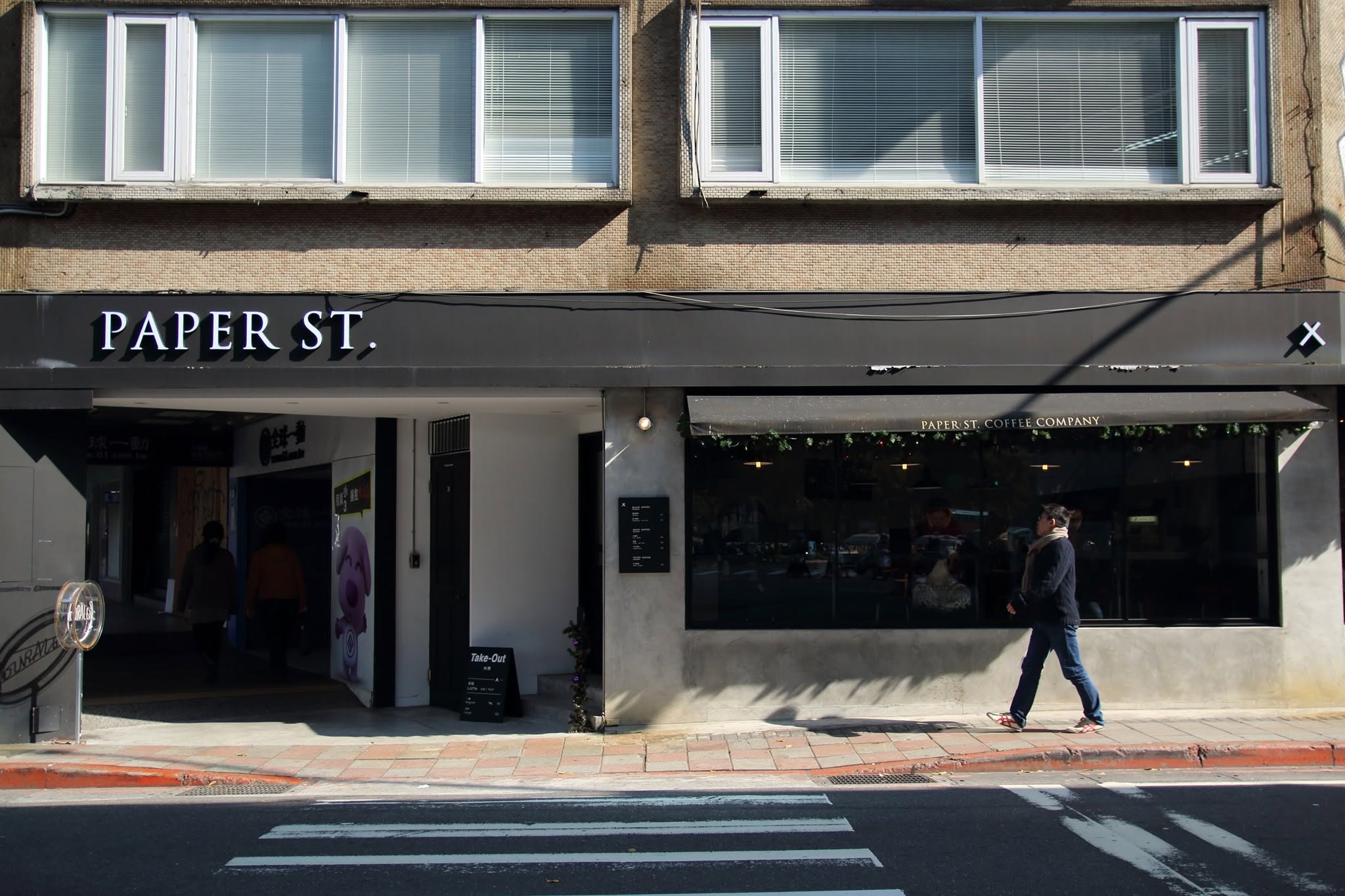 The corner storefront of Paper St. Coffee Company with raised PAPER ST. lettering above a wide street level window onto the cafe
