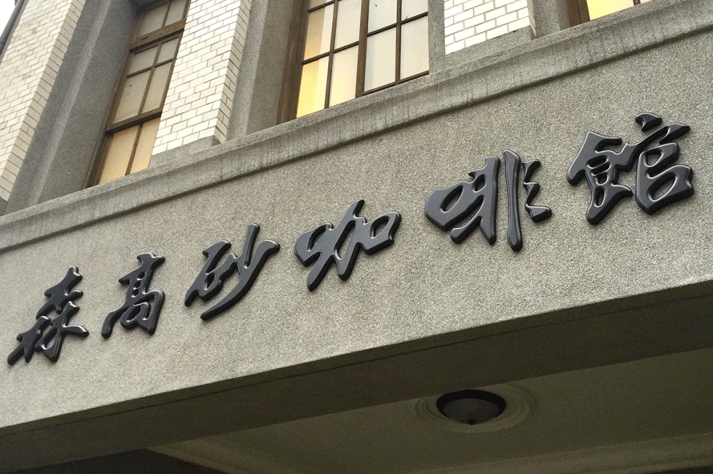 The grey stone facade of SanFormosan Coffee's 1930s Dadaocheng building, with raised black Chinese lettering reading 森高砂咖啡館 beneath white tiled columns and arched windows