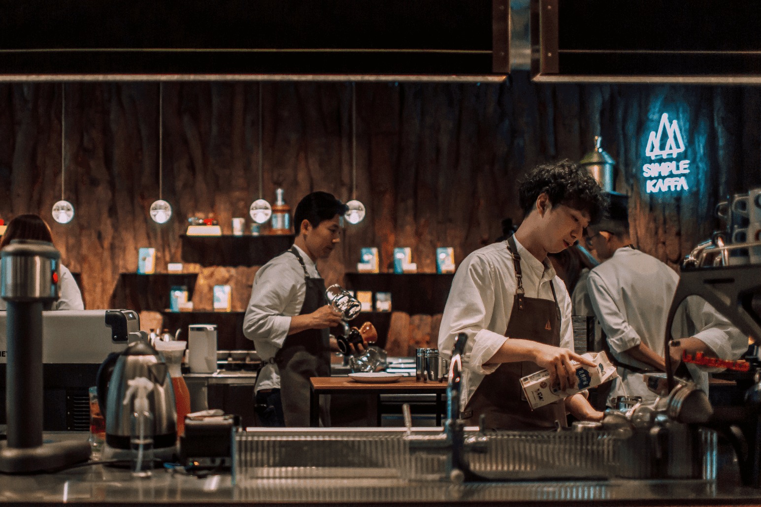 Baristas at work behind the marble bar at Simple Kaffa's Zhongzheng flagship, a glowing SIMPLE KAFFA sign on the dark wood wall behind them
