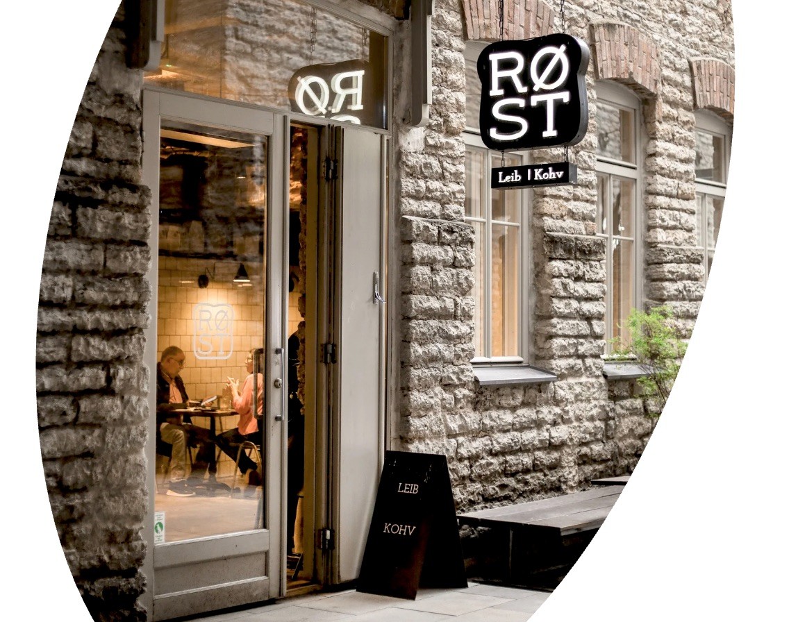 The stone facade and lit RØST sign above the open doorway of the cafe on a Tallinn street