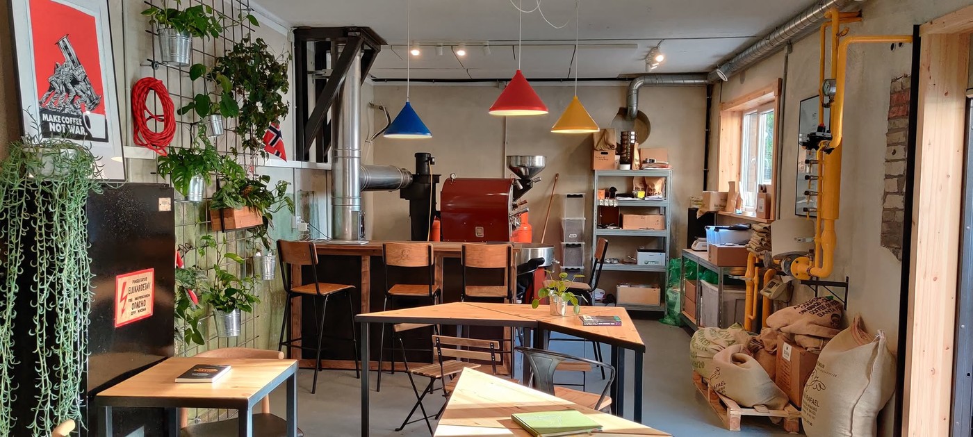The roastery floor at The Brick, with a red drum roaster, colorful pendant lights, and burlap sacks of green coffee