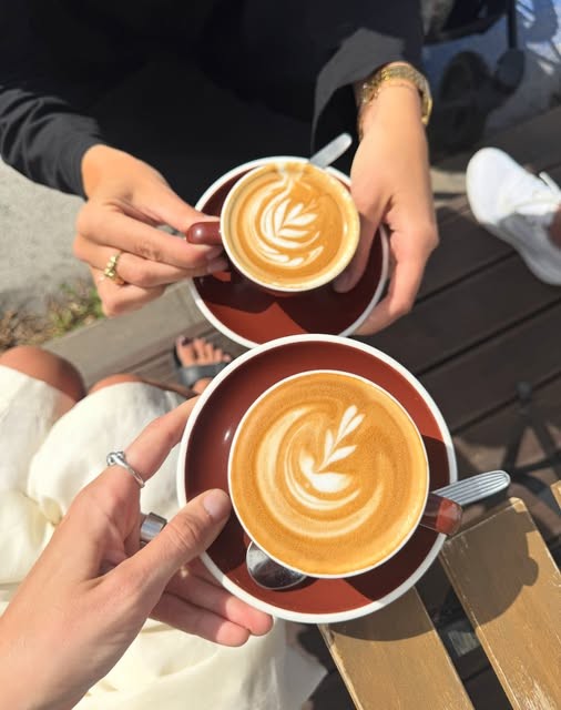 Two hands holding lattes with heart art outdoors at Värav Coffee and Toast