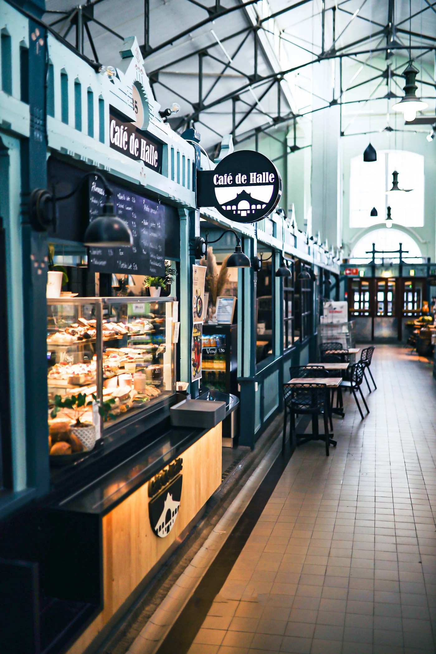The glass fronted pastry case and hanging sign of Café de Halle inside Tampere's iron roofed Market Hall