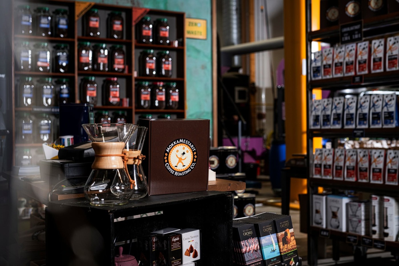 A Chemex and branded MokkaMestarit box on a counter beside shelves of retail coffee jars