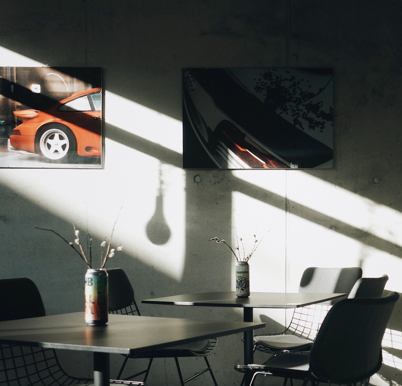 Sunlight cutting across concrete walls and black cafe tables at Kafe, with framed art prints and canned drinks left on the tabletops