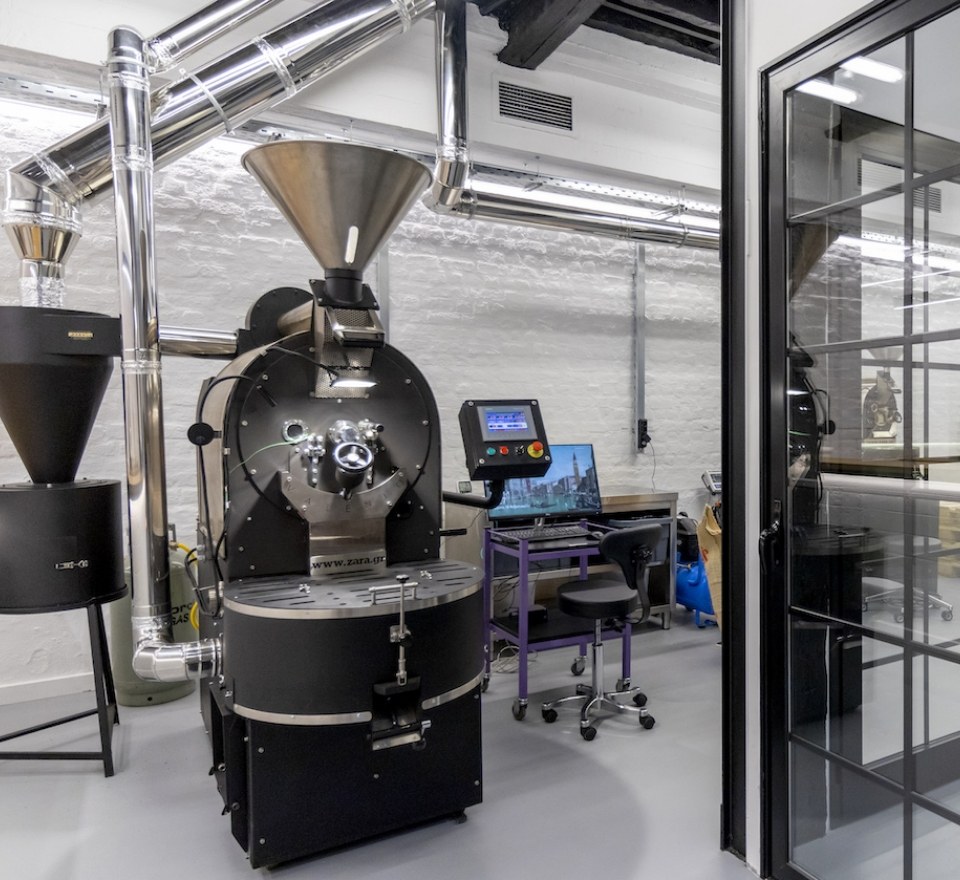 The industrial roasting machine at Valenio's Ladadika workshop, exposed brick walls and stainless steel ducting overhead