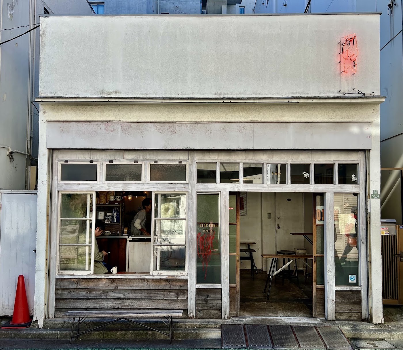 The weathered white facade of Bear Pond Espresso with a glowing neon bear sign above the open window counter