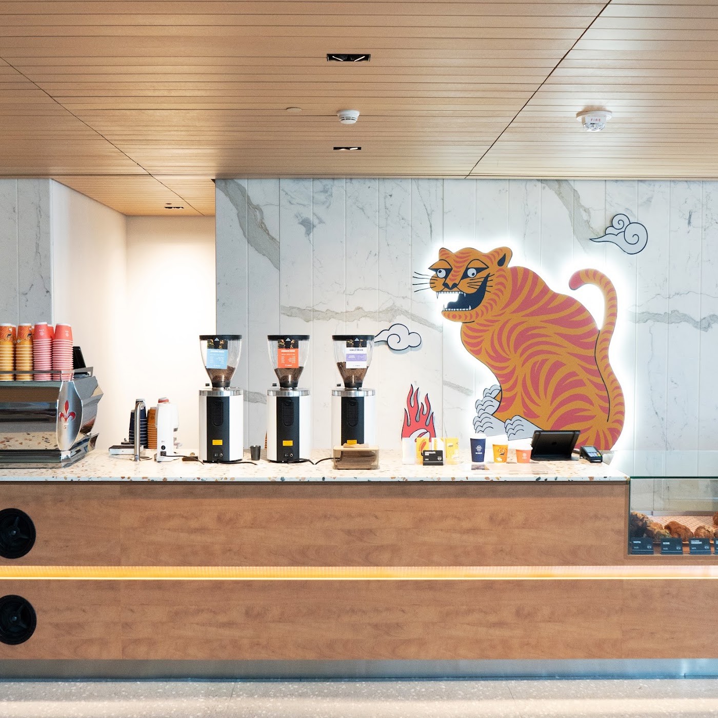 The backlit tiger mural above the espresso counter at De Mello, grinders and retail cups lined up on the terrazzo bar