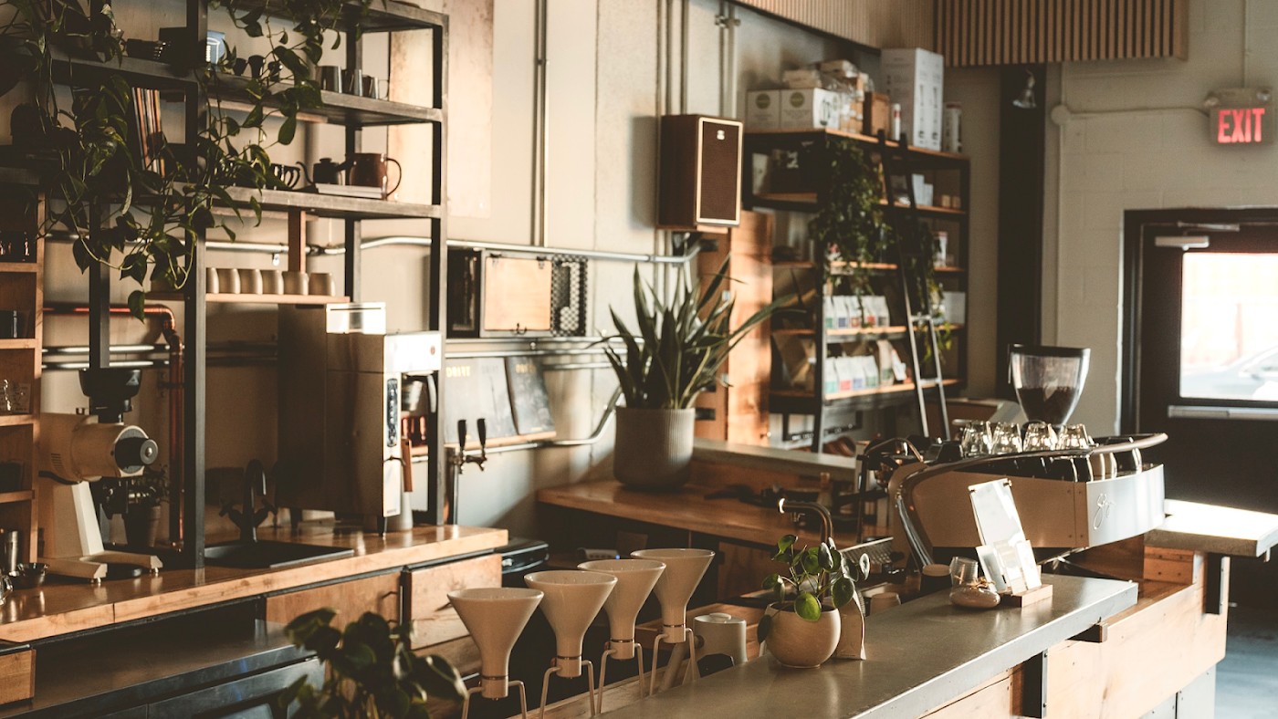 A row of pour over cones lined up on the counter at Subtext, with plants, retail bags, and the espresso machine behind