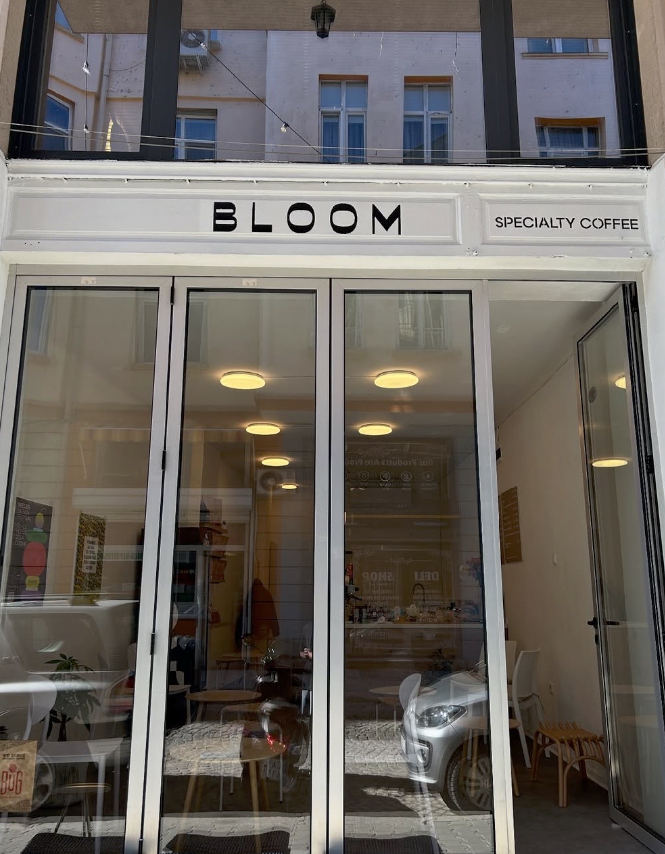 The BLOOM Specialty Coffee entrance with glass folding doors open to the interior, cafe tables visible inside
