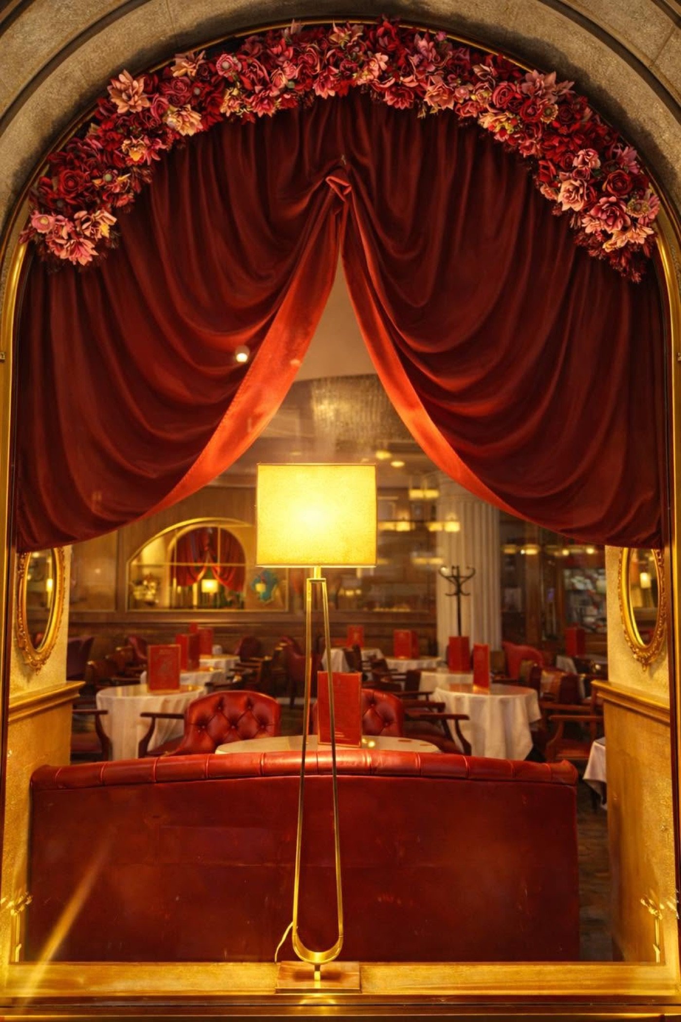 A red velvet curtain and floral arch framing the dining room at Caffè degli Specchi, tables set beneath ornate mirrors