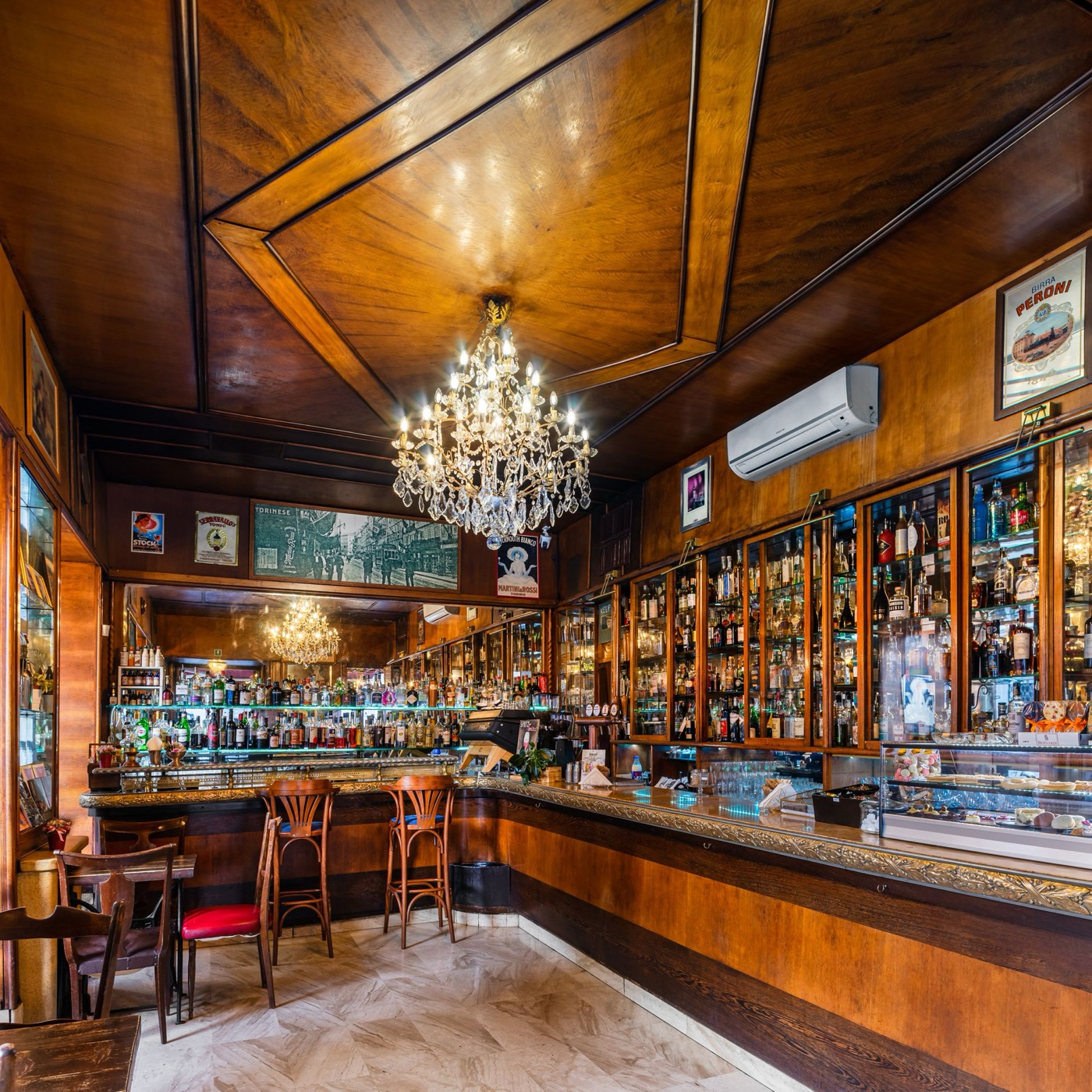The wood paneled interior of Antico Caffè Torinese, a crystal chandelier over the bar and shelves stocked with bottles