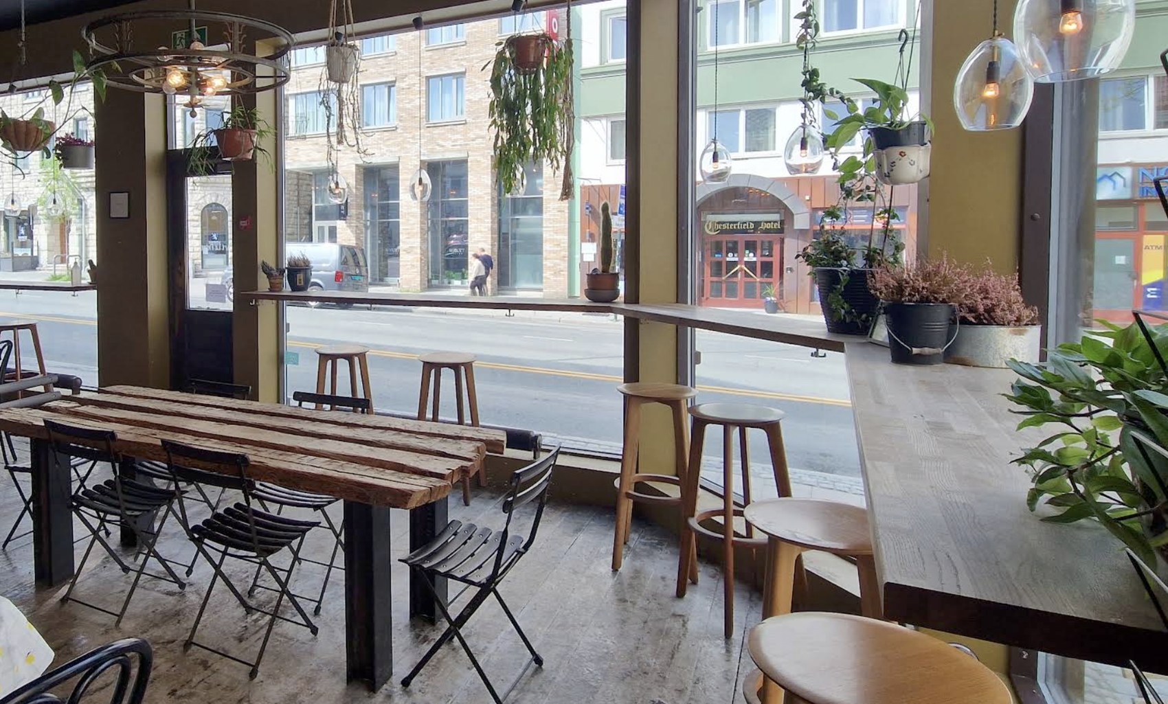 The window side seating area with hanging plants and bar stools at Cafe le Frere