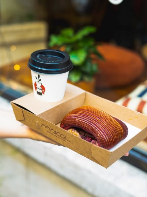 A takeaway coffee cup and a pastry in a branded box held outside Oishii Coffee