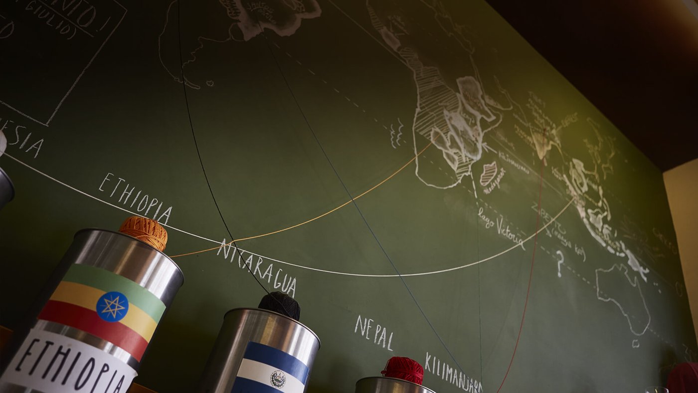 A chalkboard world map tracing coffee origins above labeled tins at Orso Laboratorio Caffe