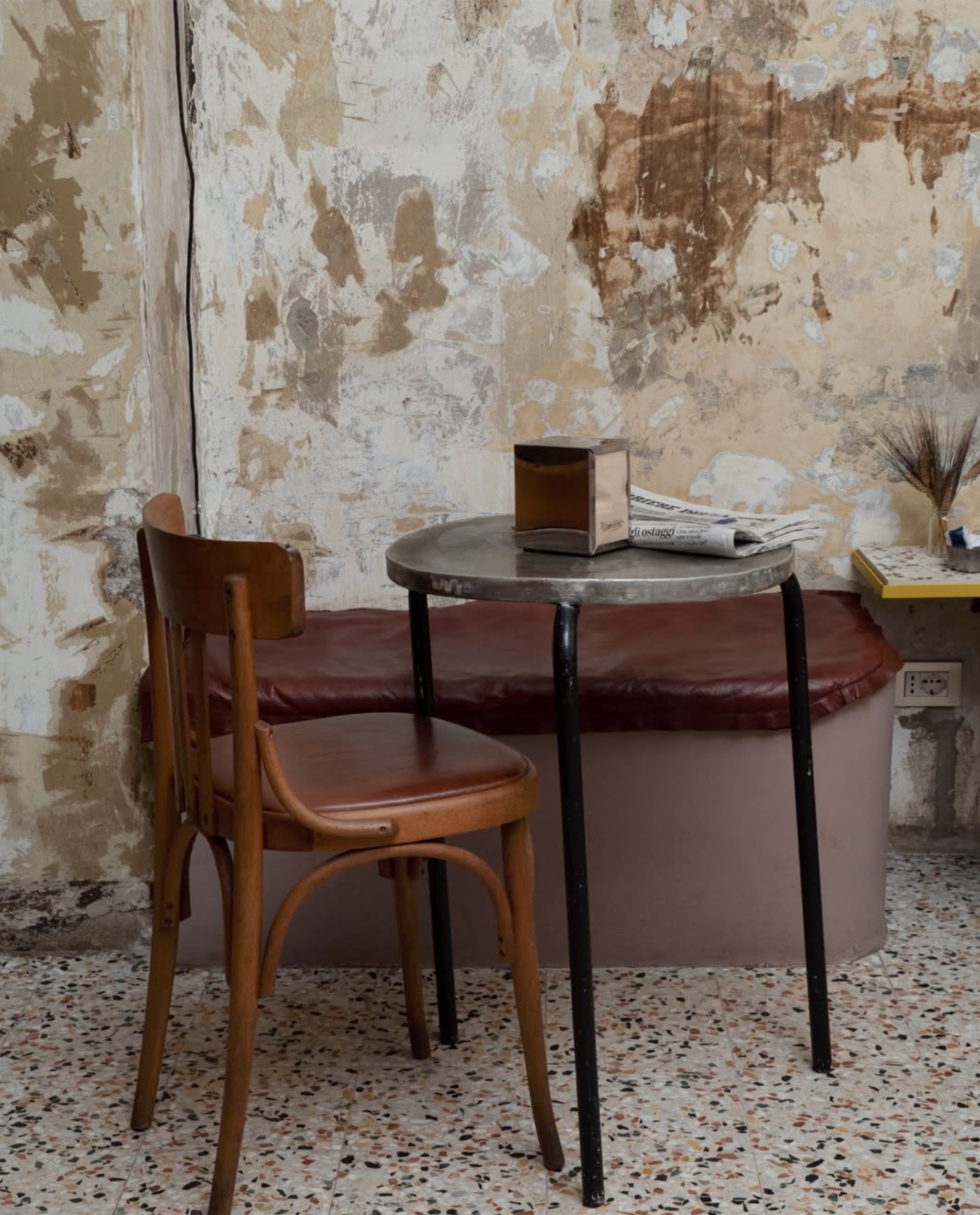 A small table and vintage bentwood chair against a weathered, peeling wall at Panificio Papale, terrazzo floor underfoot