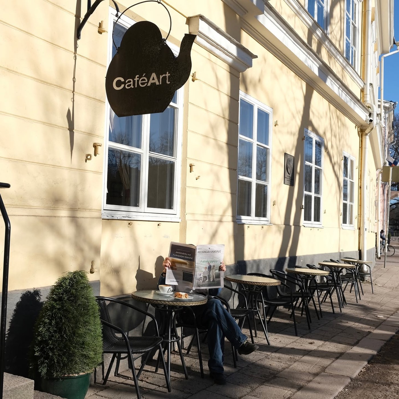 The CaféArt teapot sign hanging above the storefront, with a customer reading a newspaper at an outdoor table below