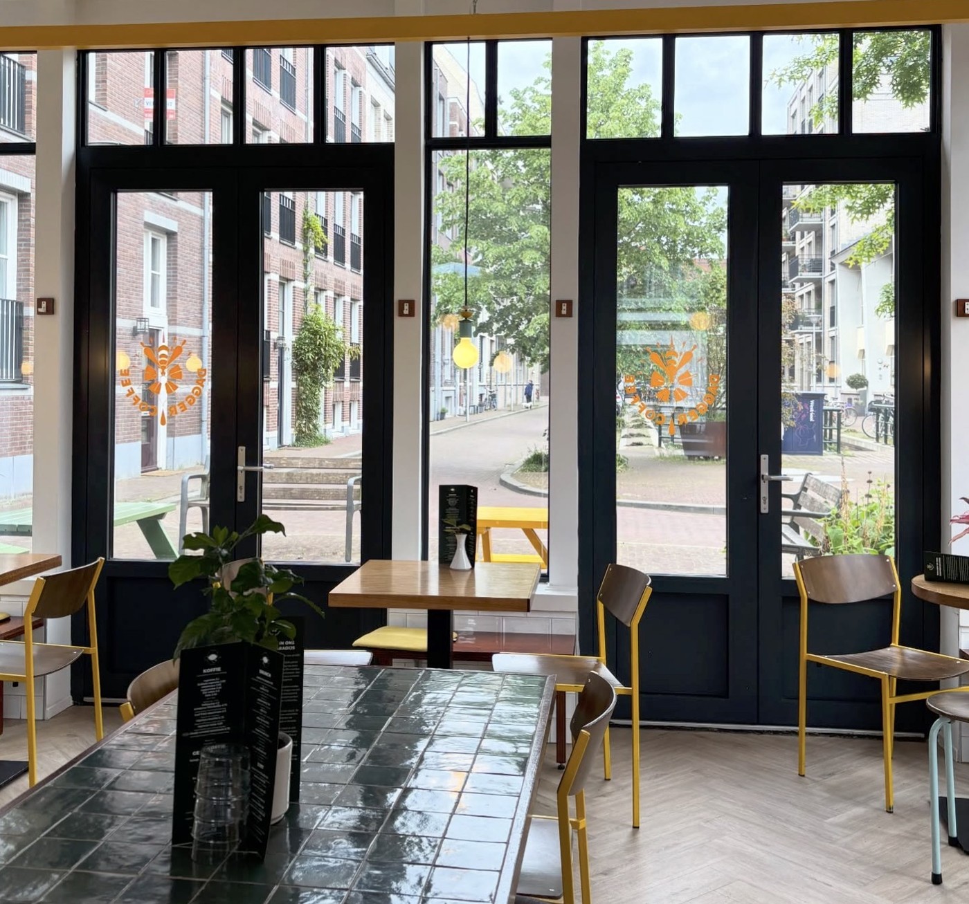Black framed doors and windows with the Dagger Coffee logo decal, opening onto wood tables and yellow chairs