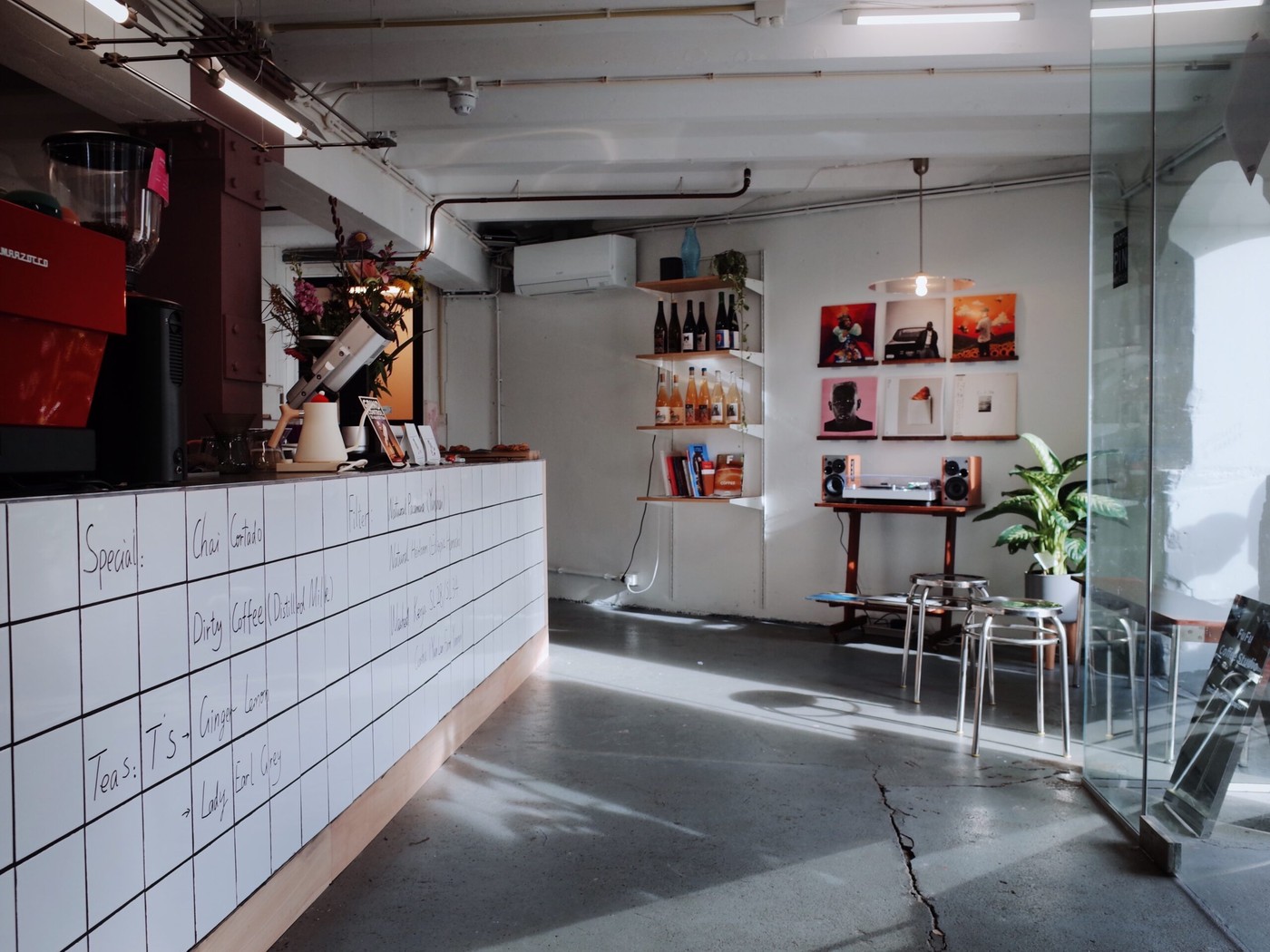 The tiled counter with a handwritten menu board and La Marzocco machine, with a record player and gallery wall in the back at Fufu Coffee Studio
