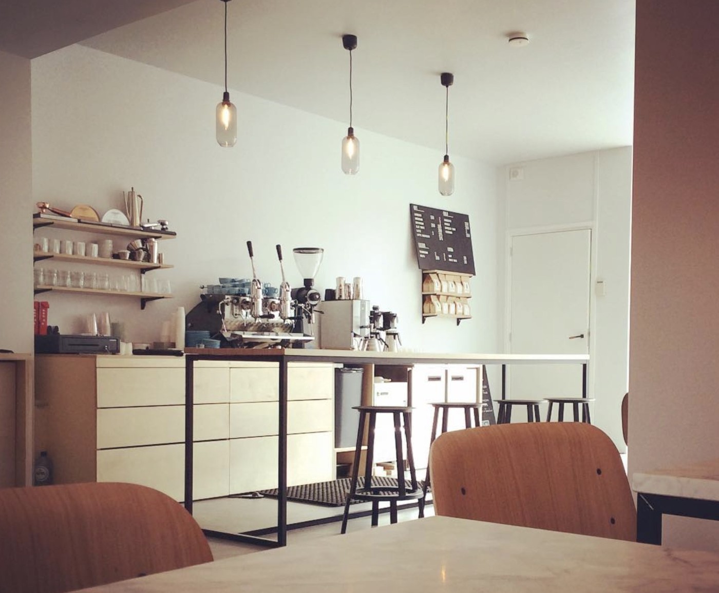 Pendant lights over the espresso bar and open shelving of cups and glassware at Ohøj
