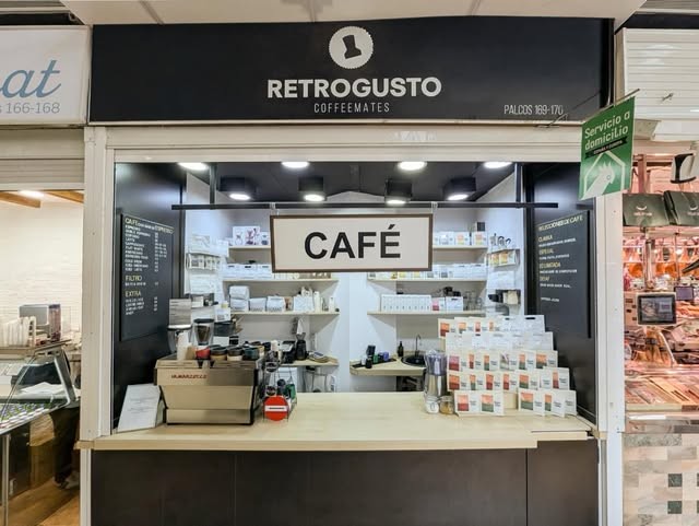 The black and white Retrogusto Coffeemates market stall with a CAFÉ sign, espresso machine, and retail bags at Mercado Central