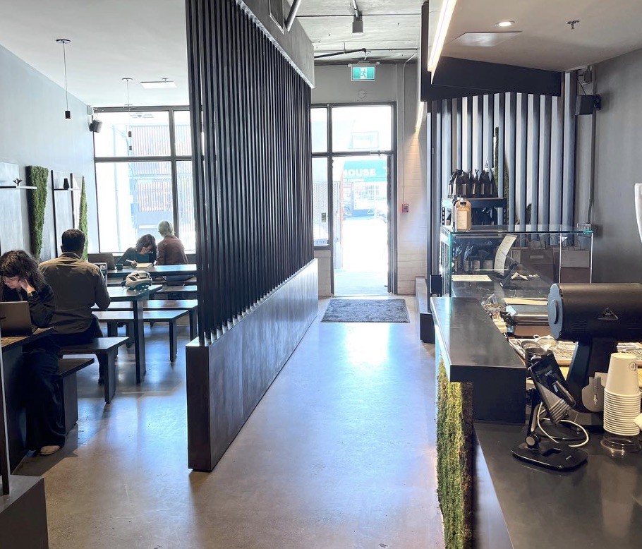 The interior of Prototype Coffee with a slatted wood divider wall, customers working at laptops on the left, and the espresso counter with a pastry case on the right